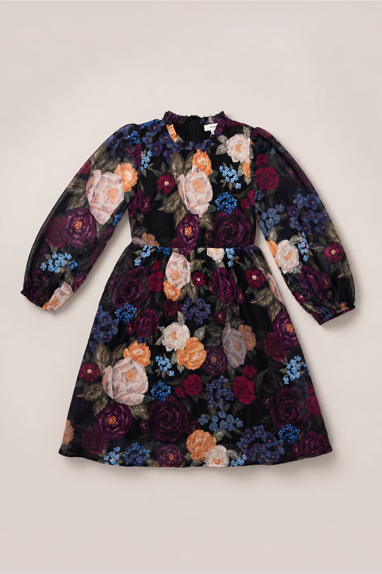 The Ivy City Co Mini Kelley Dress in Winter Floral features long sleeves, a gathered waist, and a ruffled collar. Adorned with a dark, multicolored floral pattern of roses and hydrangeas, this dress is perfect for holiday portraits or as your go-to winter floral piece. Shown here on a neutral background.