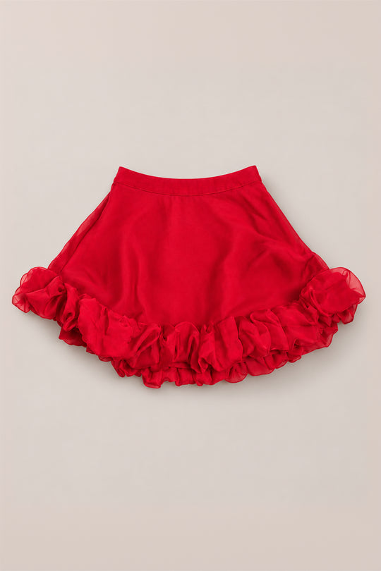 The Mini Kendy Skirt in Poinsettia by Ivy City Co is a bright red girls’ A-line skirt featuring a fitted waistband and ruffled hem, shown flat on a neutral background—making it the perfect organza skirt for your next holiday party outfit.