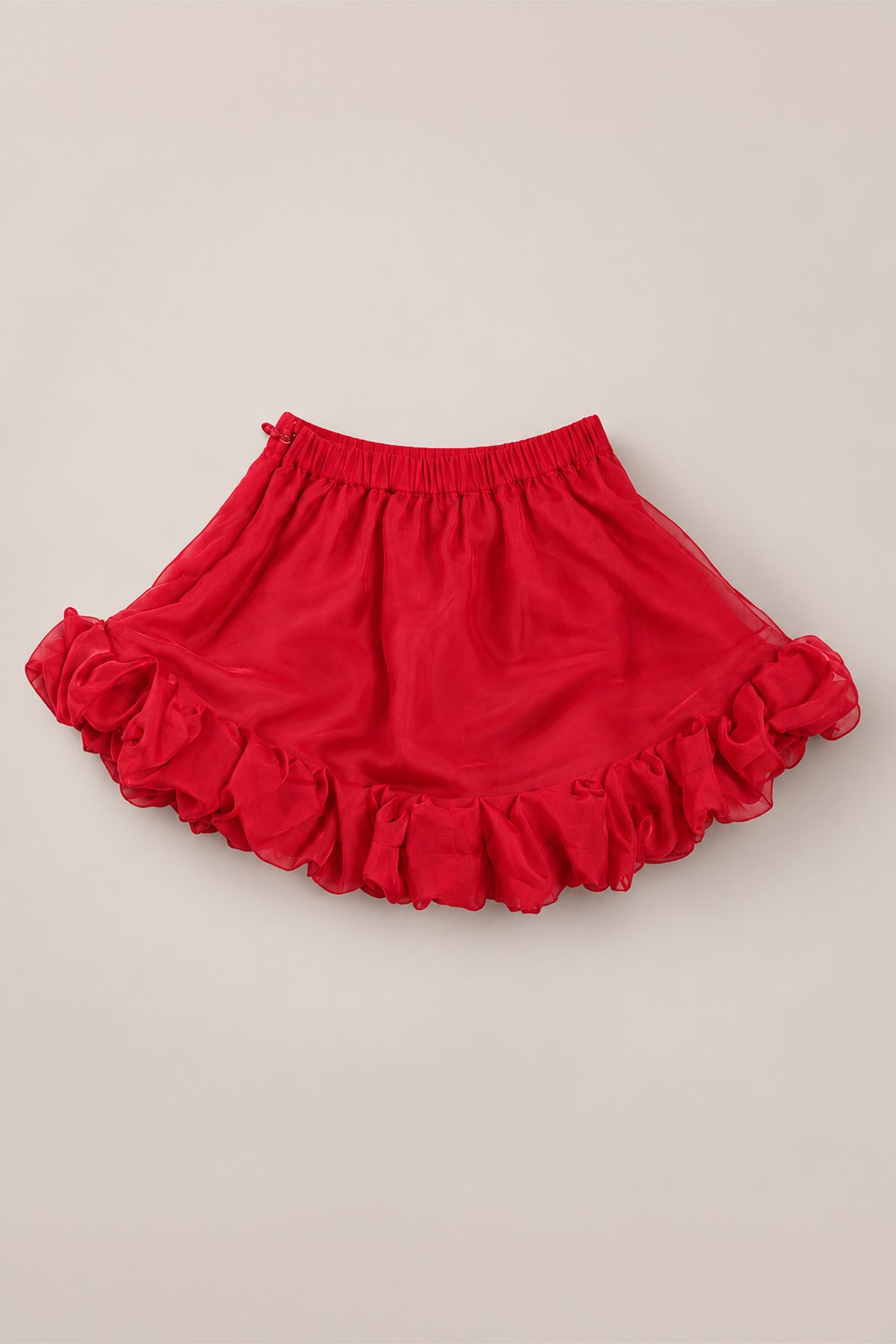 The Ivy City Co Mini Kendy Skirt in Poinsettia features a vibrant poinsettia-red organza fabric with a ruffled hem and an elastic waistband, shown laid flat on a light beige background—an ideal choice for a festive holiday party look or a charming A-line skirt for girls.
