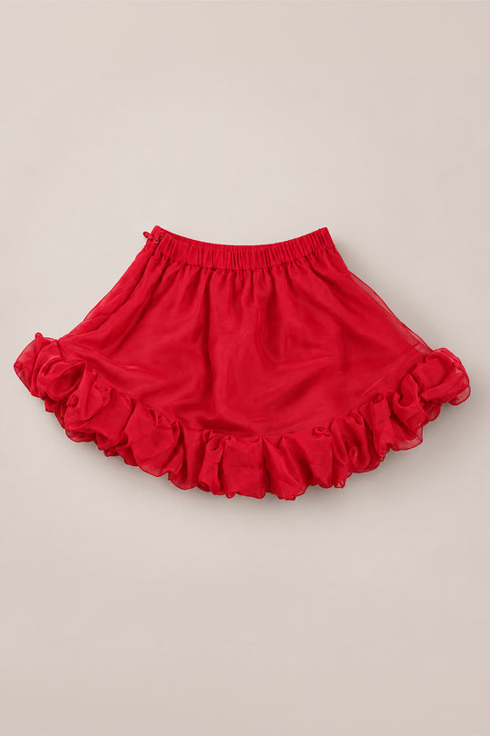 The Ivy City Co Mini Kendy Skirt in Poinsettia features a vibrant poinsettia-red organza fabric with a ruffled hem and an elastic waistband, shown laid flat on a light beige background—an ideal choice for a festive holiday party look or a charming A-line skirt for girls.