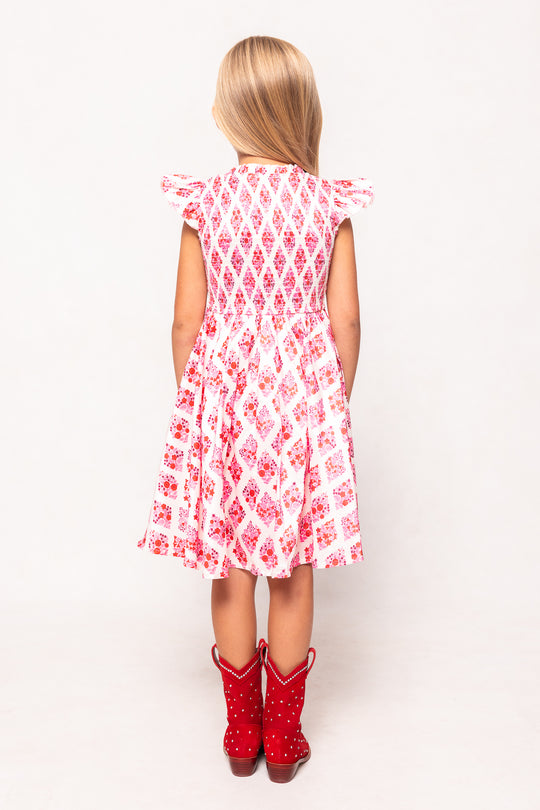 Young girl wearing a red and white patterned dress with matching boots on a white background