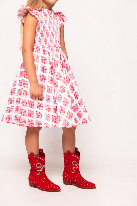 Child wearing a red and white floral dress with red cowboy boots on a white background