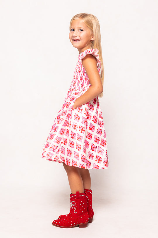 Young girl wearing a red and white checkered dress with red boots on a white background