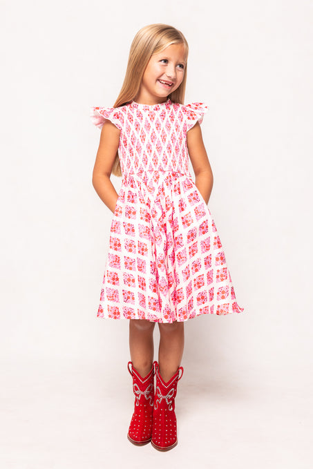 Young girl wearing a red and white patterned dress with red cowboy boots on a white background