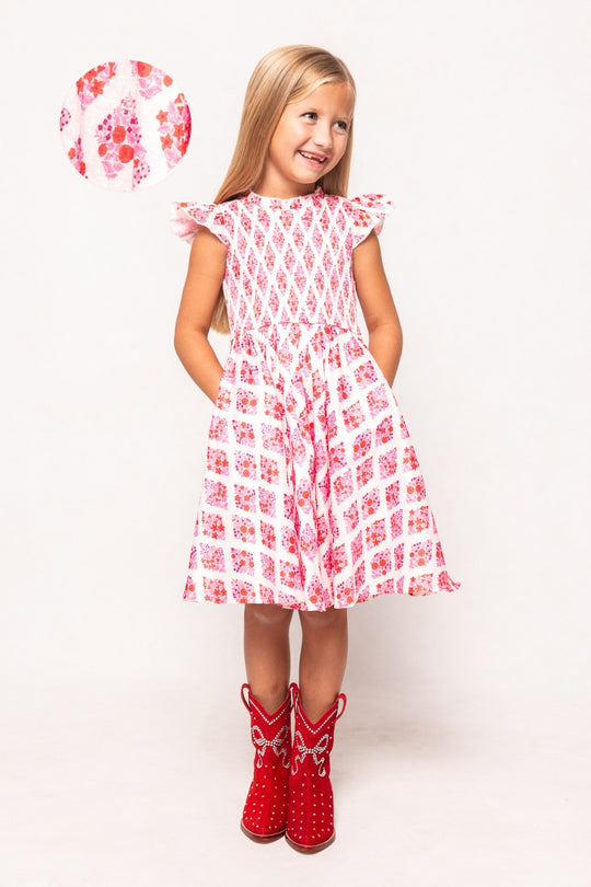 Young girl wearing a red and white patterned dress with matching boots on a white background