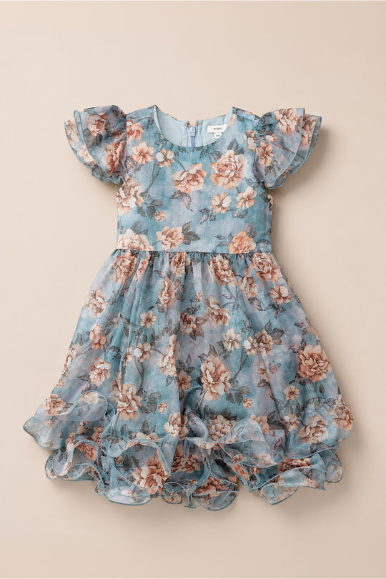 The Mini Lisette Dress in Rose Dusk by Ivy City Co features a pink and peach rose pattern with blue floral accents, short ruffled sleeves, a full ruffled skirt, and a fitted bodice with a back zipper. Perfect as a junior bridesmaid dress for a fall wedding.
