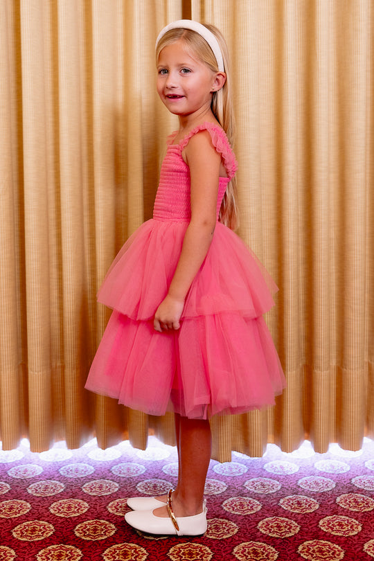 Young girl in a pink dress standing in front of a curtain.