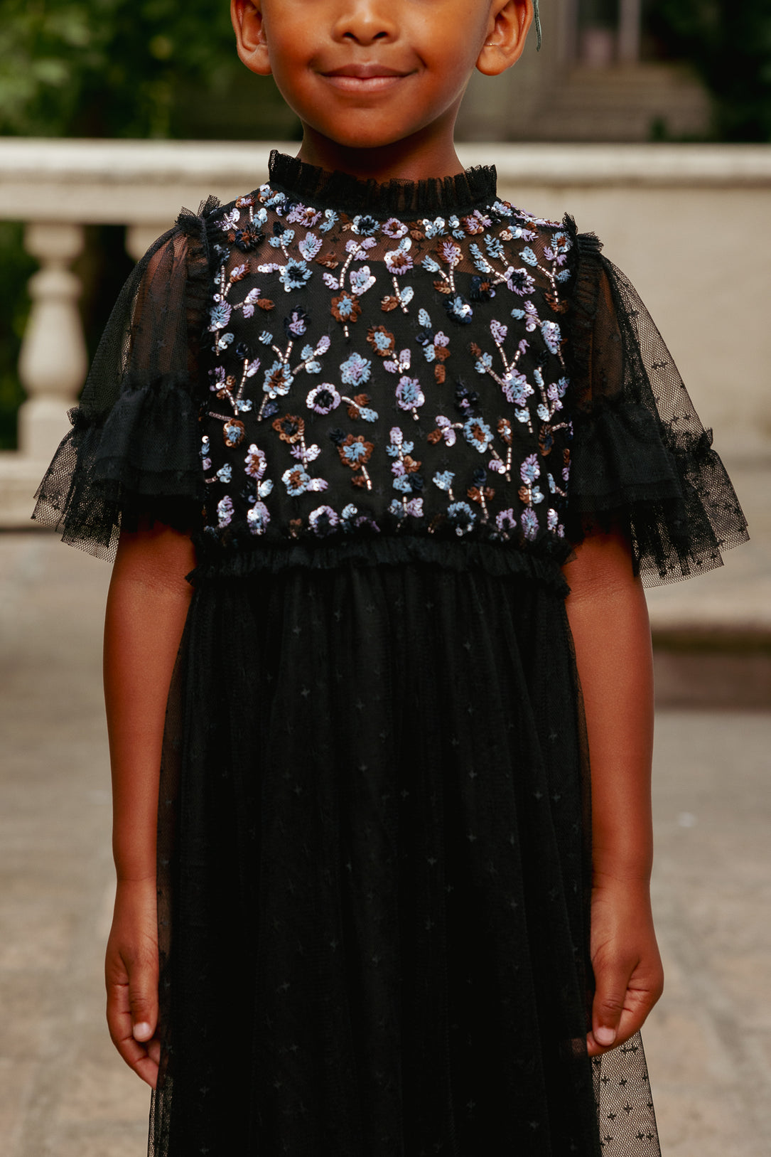 Child wearing a black dress with floral embroidery in an outdoor setting