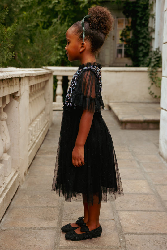 Young girl in a black dress standing on a stone path with greenery in the background