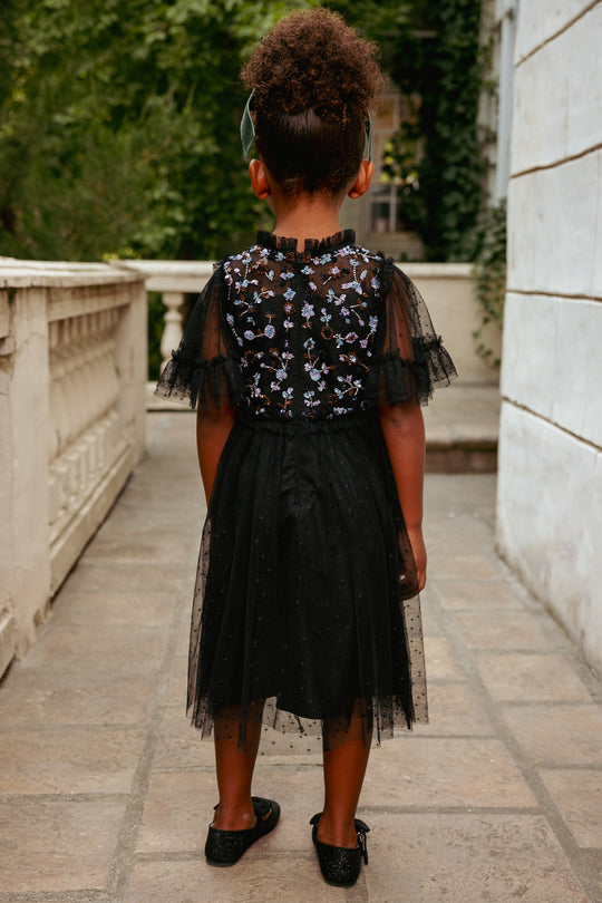 Person wearing a black floral dress with sheer sleeves in an outdoor setting.