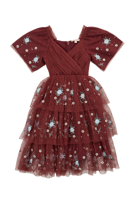 The Mini Mabel Dress in Burgundy by Ivy City Co is a girls’ formal dress with a layered tulle skirt, blue and white floral embroidery, V-neck, and puffed sleeves.