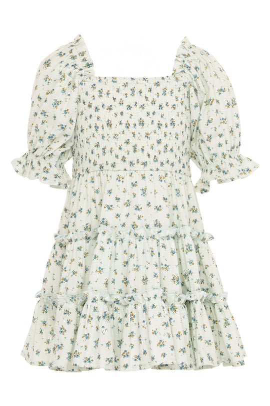 The Mini Madeline Dress in Blue by Ivy City Co features a light blue, knee-length design with a square neckline, smocked bodice, tiered skirt, ruffled details, and a small blue and green floral print for a delicate summer look.