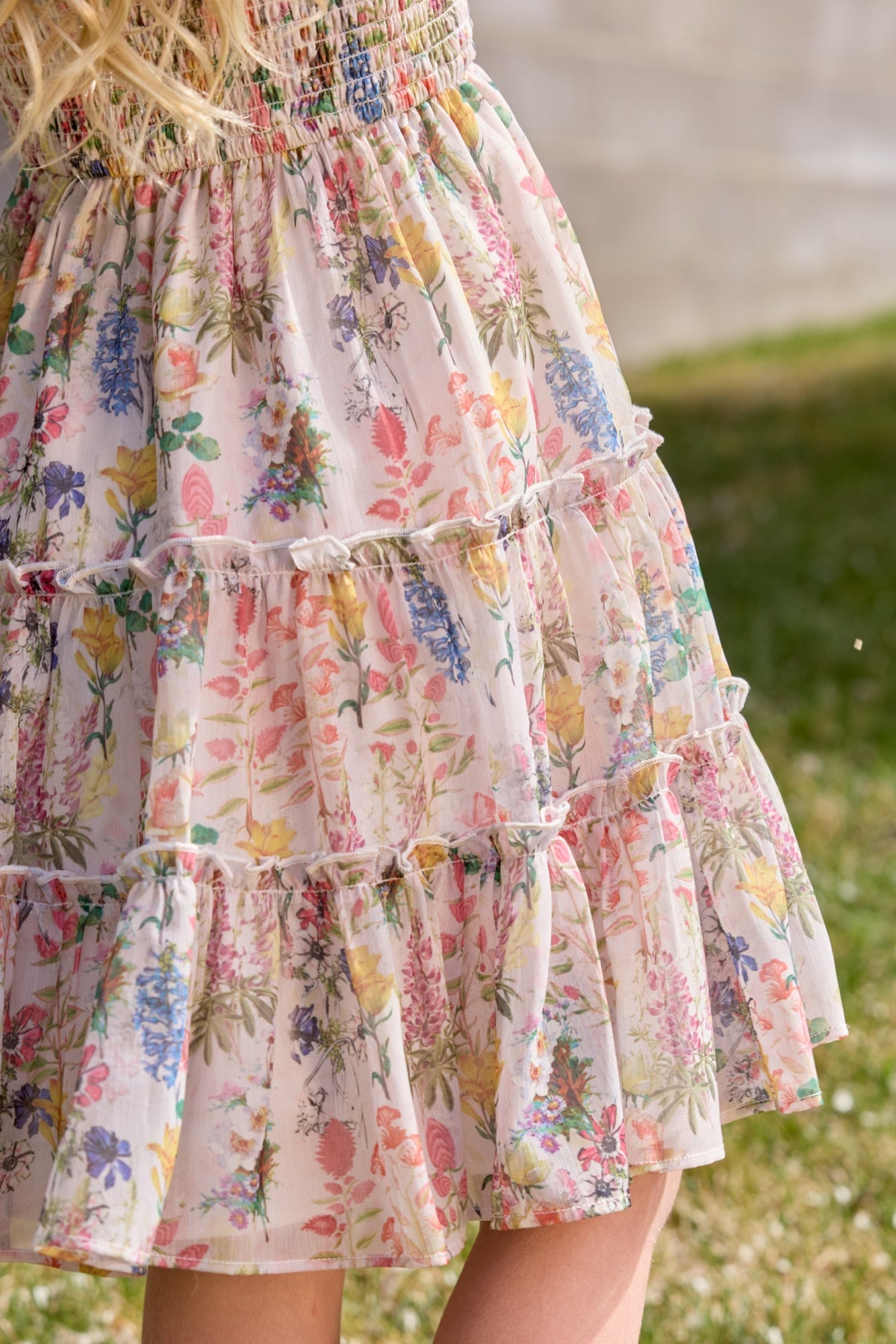 Close-up of the Ivy City Co Mini Madeline Dress in Cordelia Floral, featuring a light ruffled skirt with pink, purple, and yellow flowers—perfect for a girl's birthday outdoors on sunny days.