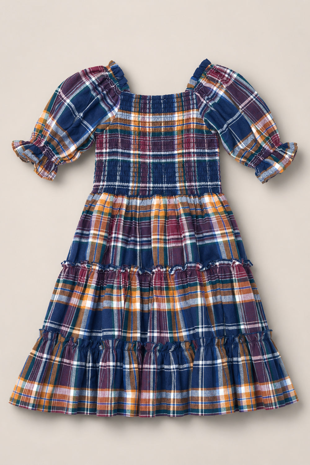 The Mini Madeline Dress in Midnight Plaid by Ivy City Co is a girls’ knee-length dress featuring ruffled tiers, puff sleeves, and a smocked bodice. Crafted from soft fabric, it showcases a multicolored plaid pattern in blue, yellow, and red tones.