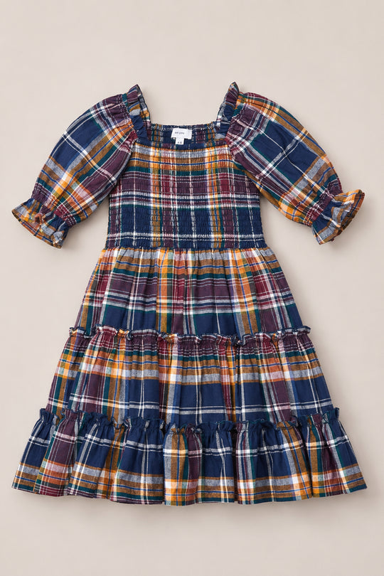 The Mini Madeline Dress in Midnight Plaid by Ivy City Co is displayed flat on a neutral background, showcasing its multicolored plaid pattern, puff sleeves, fitted smocked bodice, and ruffled tiered skirt.