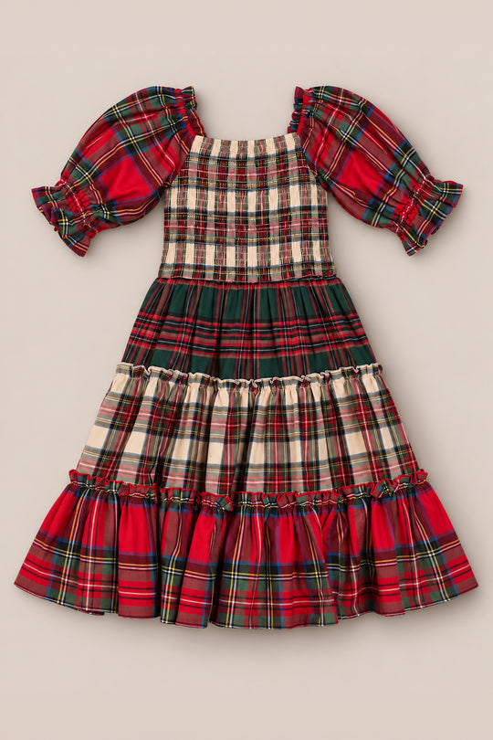 The Mini Madeline Dress in Mixed Plaid by Ivy City Co is a delightful girls’ plaid dress with puff sleeves and a ruffled hem, showcasing festive red, green, and cream patchwork patterns on a neutral background—making it the perfect Christmas dress for the holiday season.