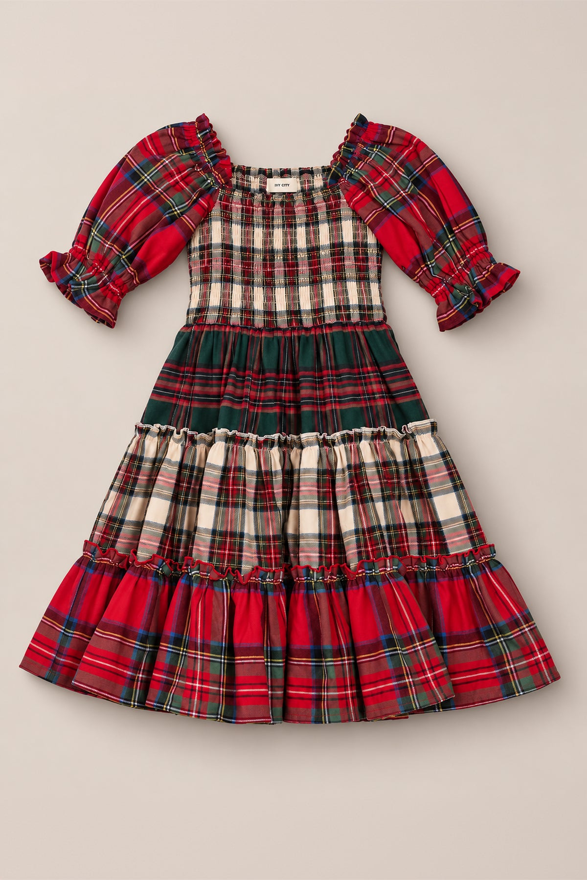 The Mini Madeline Dress in Mixed Plaid by Ivy City Co features puffed sleeves and a tiered skirt in a variety of red, green, and white plaid patterns. With its charming smocked bodice, this dress offers a festive and classic look—perfect as a Christmas dress for holiday celebrations.