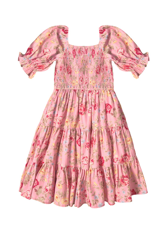 The Mini Madeline Dress in Pink Vintage Poppies by Ivy City Co is a girls’ spring dress featuring puffed sleeves, a square neckline, smocked bodice, tiered skirt, and red, yellow, and blue vintage poppies on a light pink background.