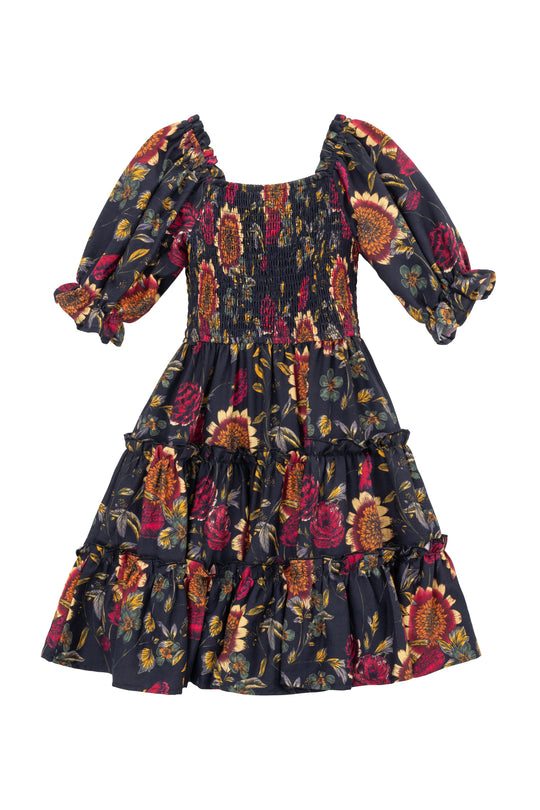 The Ivy City Co Mini Madeline Dress in Moody Sunflower features a dark floral print with red, yellow, and orange blooms on black, a smocked bodice, puffed half sleeves, and a tiered ruffle skirt—perfect for girls.