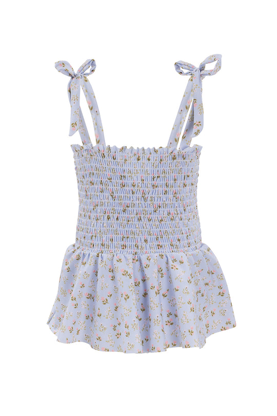 The Mini Maggie One Piece in Blue Ditsy Floral by Ivy City Co features a light blue ditsy floral print, smocked bodice, peplum hem, and adjustable tie straps for a custom fit.