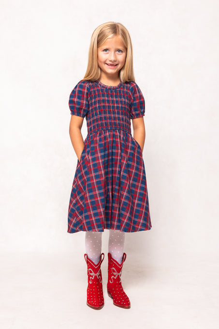 Young girl wearing a red and blue plaid dress with red boots on a white background