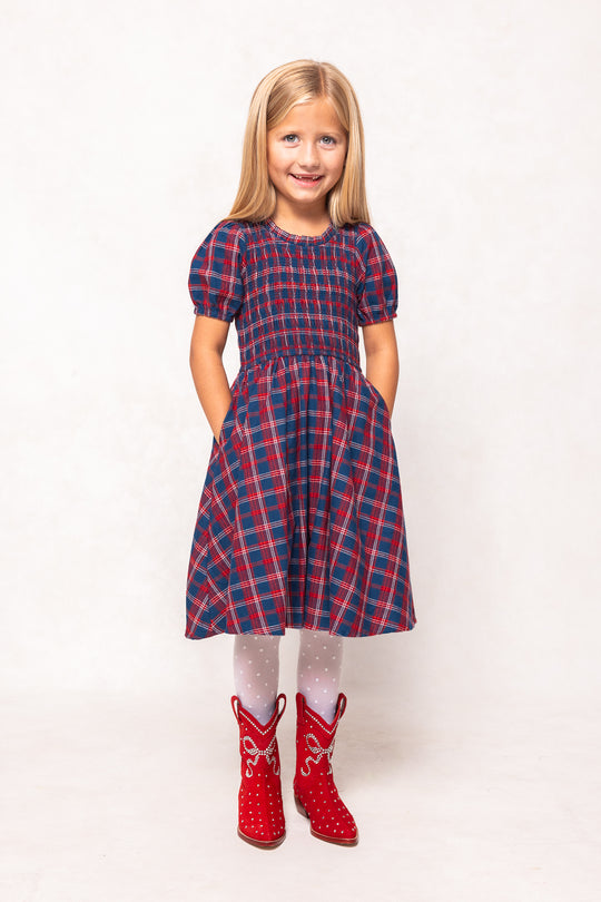 Young girl wearing a red and blue plaid dress with red boots on a white background