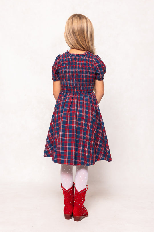 Person wearing a red and blue plaid dress with white tights and red boots on a white background