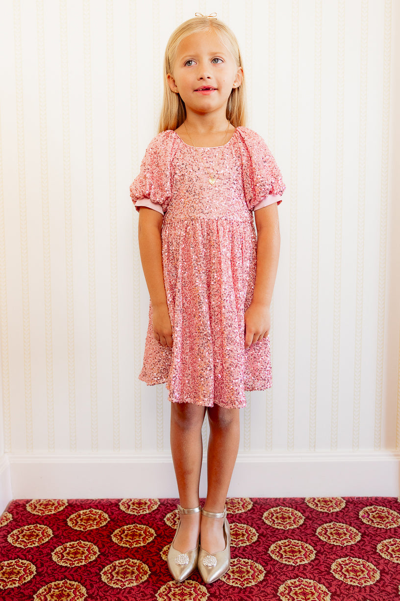 Little girl in a Pink sequin dress against a white wall standing on a red carpet