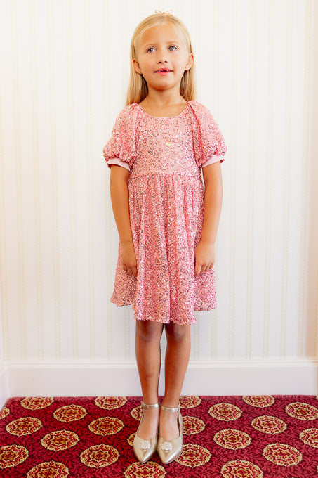 Little girl in a Pink sequin dress against a white wall standing on a red carpet