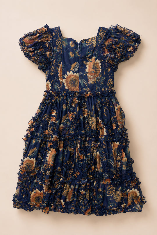 The Mini Marseille Dress in Sunflower Twilight by Ivy City Co is a navy blue, short-sleeved, ruffled dress with a sunflower and floral pattern, featuring a fitted bodice and tiered skirt—perfect for girls as a holiday dress on enchanting sunflower twilight evenings.