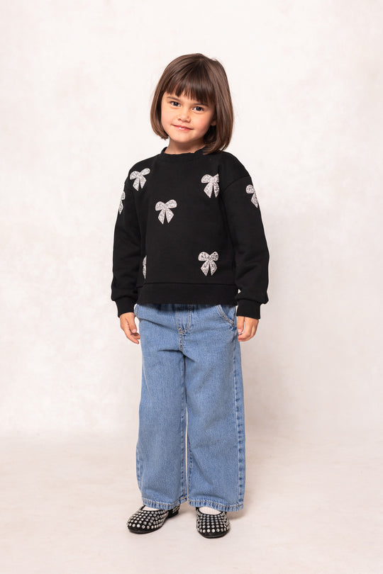 child in a black sweatshirt and jeans against a white background