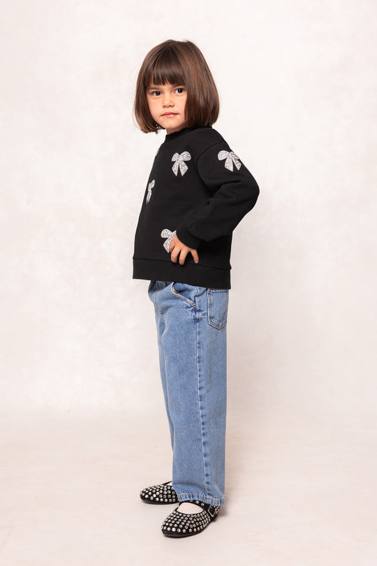 child in a black sweatshirt and jeans against a white background