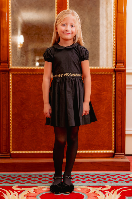 little girl in a black dress standing on a colorful carpet. 