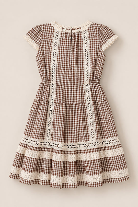 The Mini Palermo Dress in Hickory Gingham by Ivy City Co features a brown and white gingham pattern with short puff sleeves, cream lace trim, and a gathered waist. This cotton-blend dress showcases vertical lace panels and a tiered skirt with lace detailing at each tier, creating a charming vintage cottagecore aesthetic.