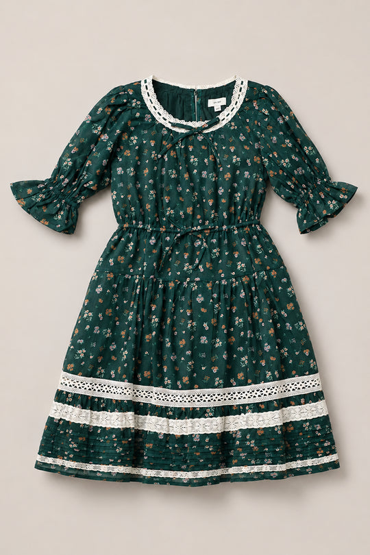 Introducing the Mini Palermo 3/4 Sleeves Dress in Evergreen Lovelorn Ditsy by Ivy City Co—a girls’ cotton dress adorned with a dark green ditsy floral print and delicate white lace accents at the neckline, cuffs, and hem. Featuring elegant 3/4 puff sleeves, a gathered waistline, and a knee-length skirt, this charming piece blends timeless florals with intricate lace details for a captivating look.