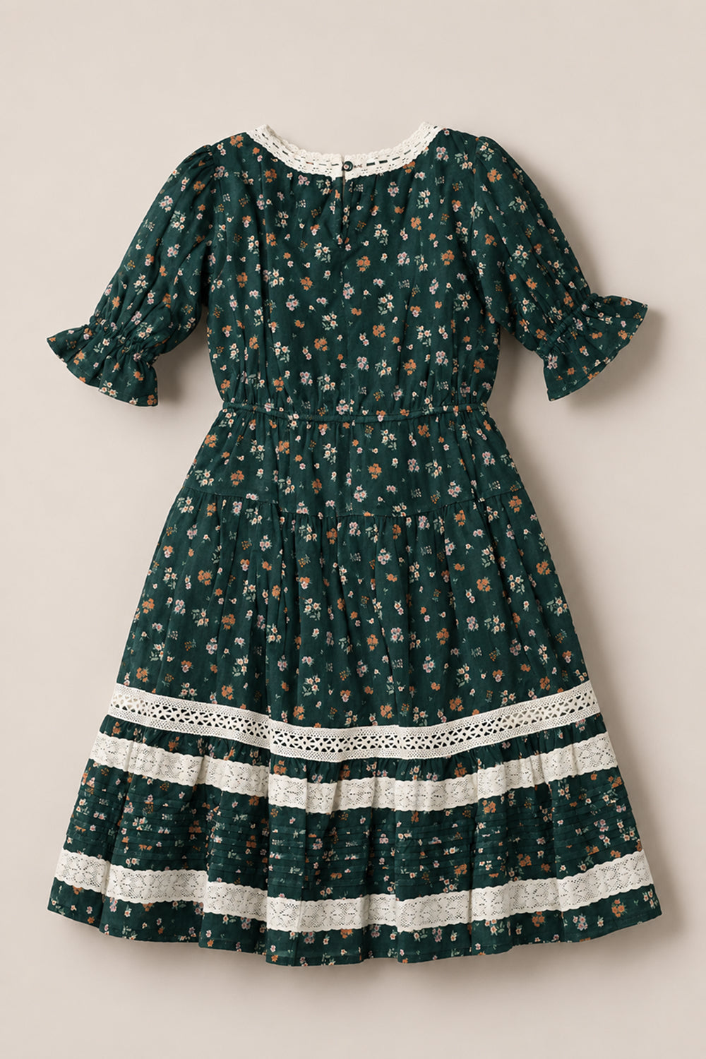 The Mini Palermo 3/4 Sleeves Dress in Evergreen Lovelorn Ditsy by Ivy City Co is a dark green girls’ cotton dress with a charming small floral pattern, puffed three-quarter sleeves, gathered waist, and white lace trim. Displayed flat on a neutral background, the skirt features horizontal lace accents—making it perfect for any occasion.