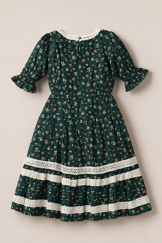 The Mini Palermo 3/4 Sleeves Dress in Evergreen Lovelorn Ditsy by Ivy City Co is a dark green girls’ cotton dress with a charming small floral pattern, puffed three-quarter sleeves, gathered waist, and white lace trim. Displayed flat on a neutral background, the skirt features horizontal lace accents—making it perfect for any occasion.