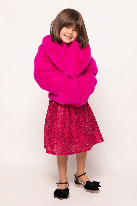Child wearing a bright pink fur coat and sequin skirt on a white background