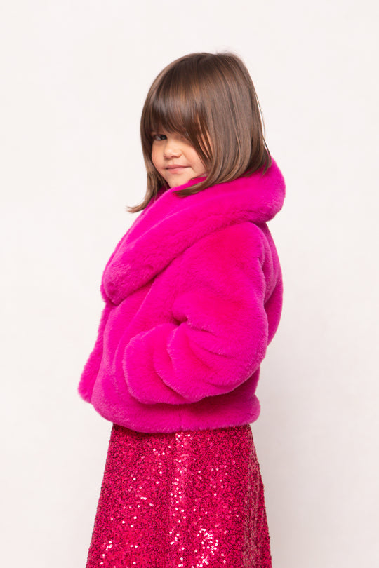 Child wearing a bright pink faux fur coat and sequin skirt on a white background