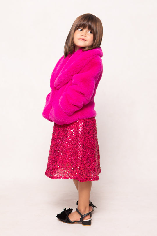 Child wearing a bright pink fur coat and sequin skirt on a white background