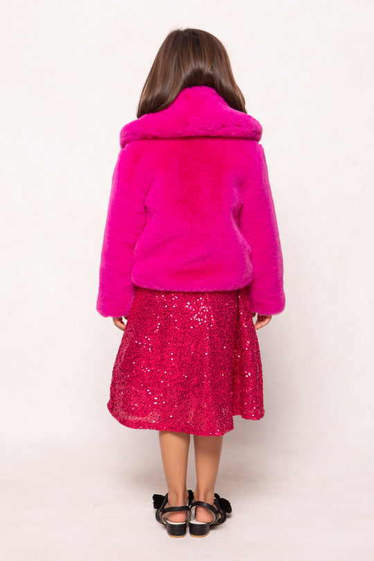 Person wearing a bright pink coat and sequin skirt on a white background