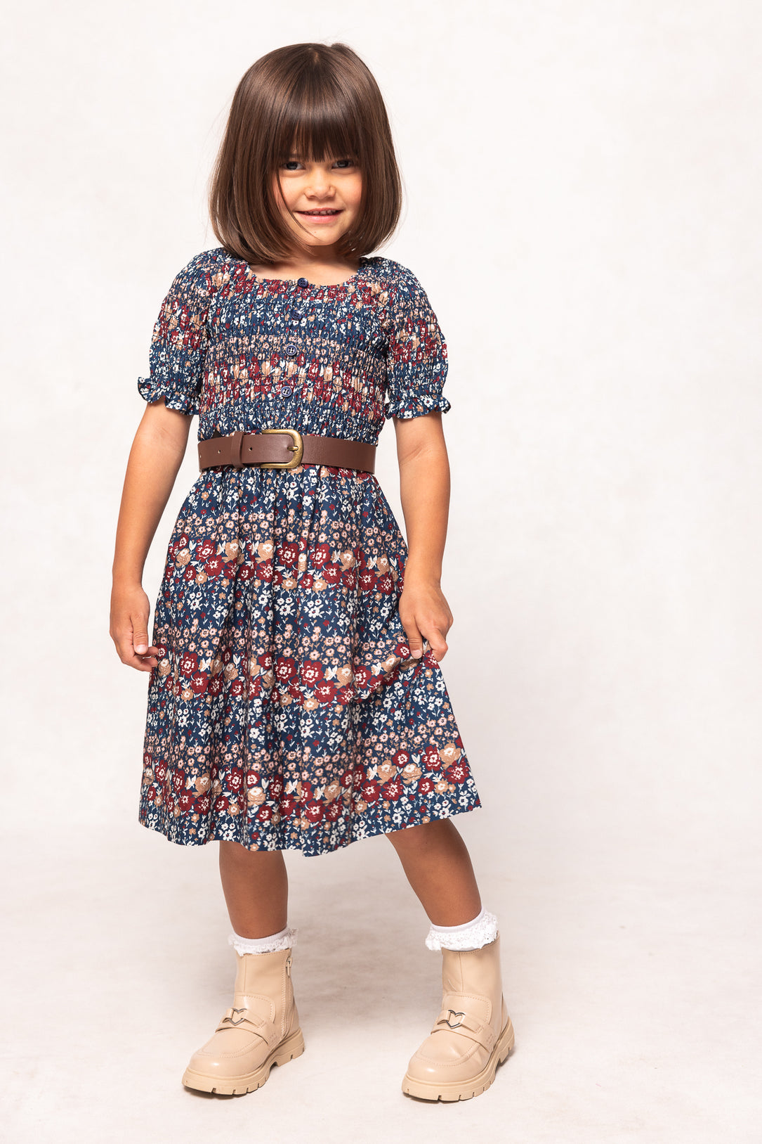 Young girl wearing a floral dress with a brown belt on a white background