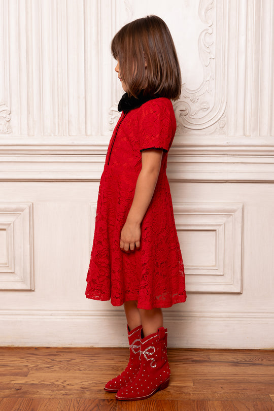 Child wearing a red dress and matching red boots against a white wall.