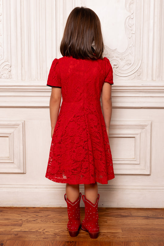 Person wearing a red lace dress and matching red boots against a white wall.
