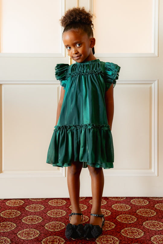 little girl in a green dress against a white wall