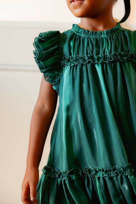 close up of a little girl in a green dress against a white wall