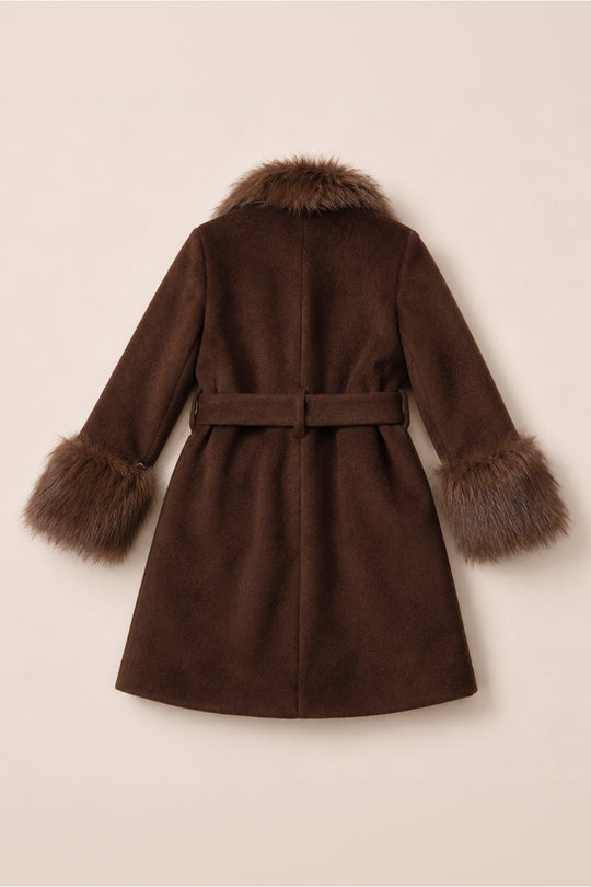 The Mini Pookie Coat in Warm Cocoa by Ivy City Co is a brown, knee-length girl’s fall coat featuring a belted waist and faux fur trim on the collar and cuffs. Displayed on a plain, light background, the coat is shown from the back—offering stylish comfort for cooler weather.