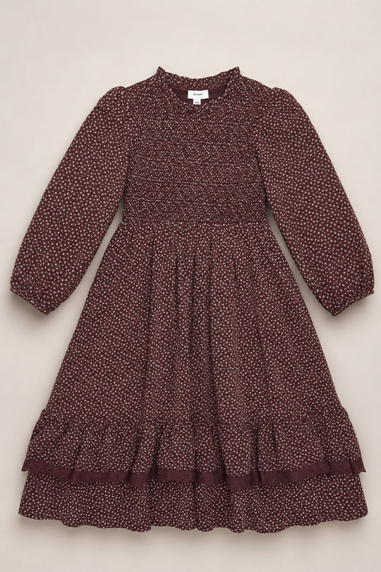 A mahogany ditsy long-sleeve dress, the Mini Presley Maxi Dress by Ivy City Co, is displayed flat on a light background. This charming piece features white polka dots, elegant balloon sleeves, a smocked bodice, ruffled hem, and a gathered skirt—perfectly capturing its playful yet refined spirit.