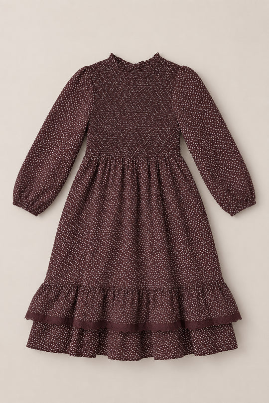 The Mini Presley Maxi Dress in Mahogany Ditsy by Ivy City Co features long balloon sleeves, a maroon background with tiny white polka dots, a smocked bodice, ruffled cuffs, and a tiered ruffle hem. The dress is shown laid flat on a neutral background.