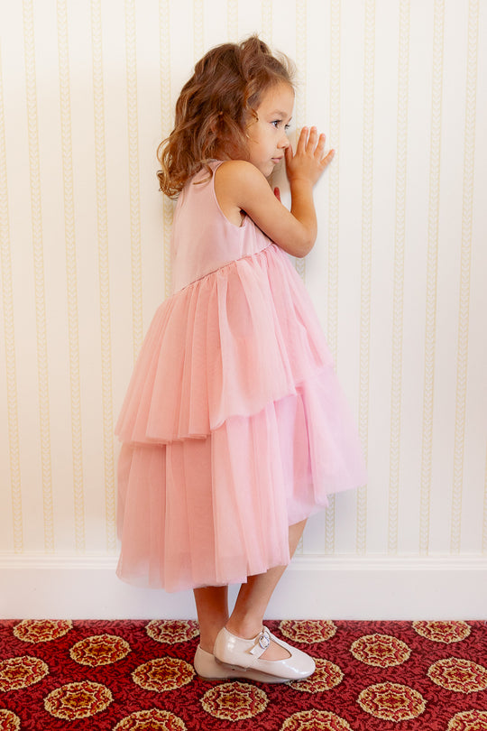 little girl in a pink dress standing against a white wall